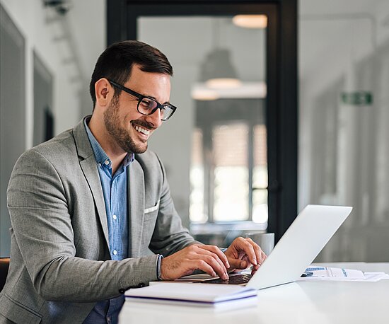 Mann arbeitet am Laptop im Büro und lacht