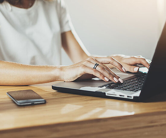 Frau sitzt an einem Schreibtisch und arbeitet auf einem Laptop