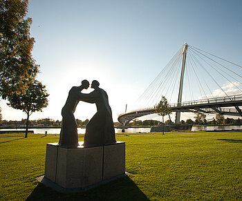 Statue auf grüner Wiese vor einer Brücke in Kehl