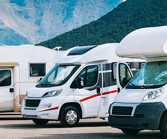 Wohnmobile auf einem Parkplatz vor der beeindruckenden Kulisse der Berge