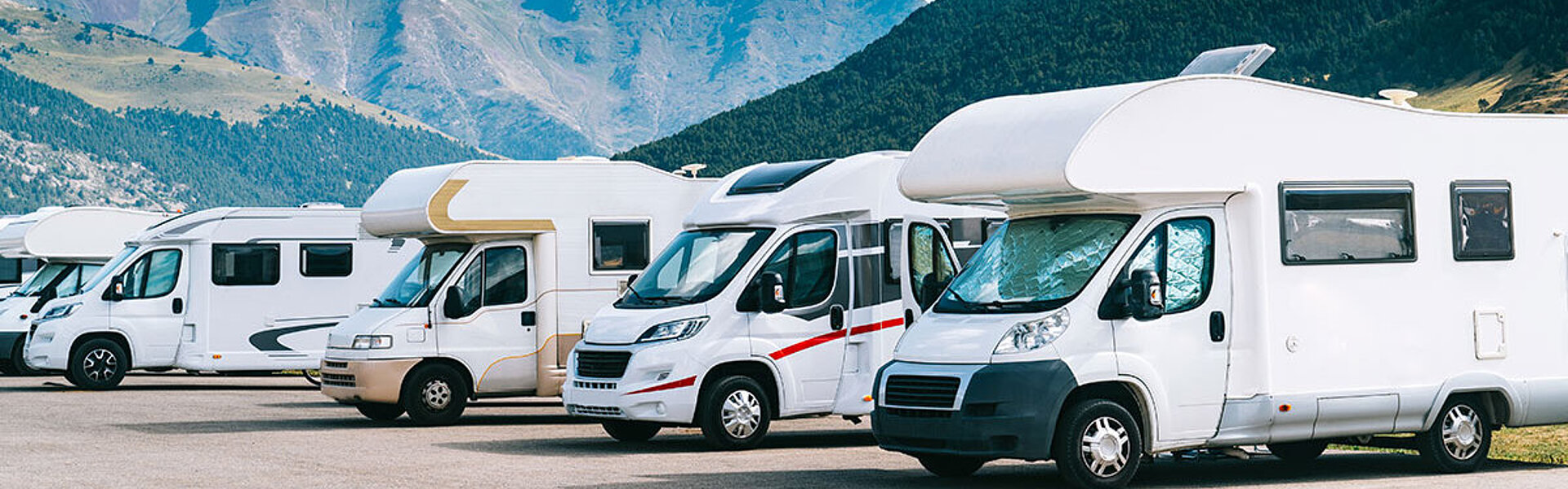 Wohnmobile auf einem Parkplatz vor der beeindruckenden Kulisse der Berge